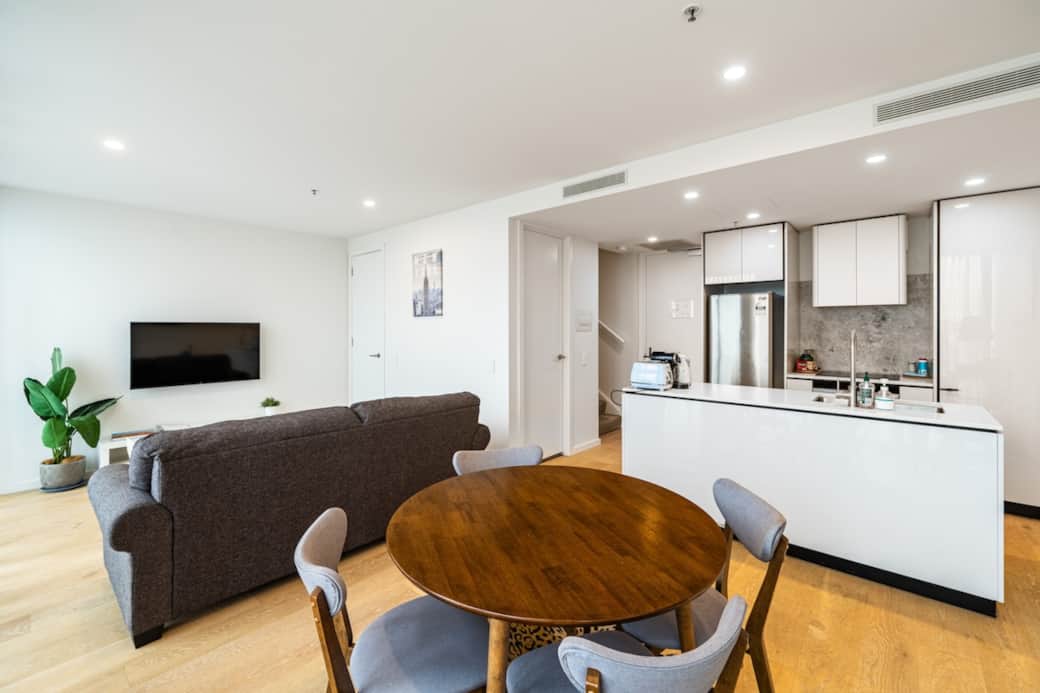 A modern living space that blends comfort with chic, featuring a plush sofa, wooden dining area, and an open kitchen, all bathed in natural light.An airy and well-appointed living room with wide windows, drawing the city into a cozy, stylish interior