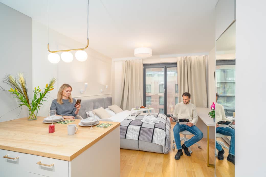 A bright studio apartment with a kitchenette, a large bed, and a balcony window.