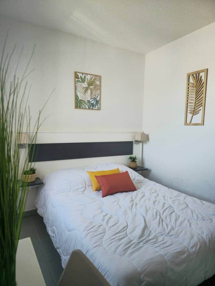 Chambre double lumineuse avec lit confortable, tables de chevet et déco végétale. Un espace cosy et apaisant, parfait pour se reposer après une journée à la plage d’Argelès-sur-Mer.