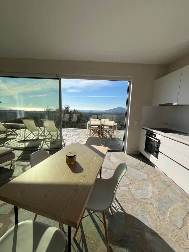 Bright living area with open kitchen and large glass doors opening onto the terrace. The table facing the landscape, indoors and outdoors in perfect continuity.
