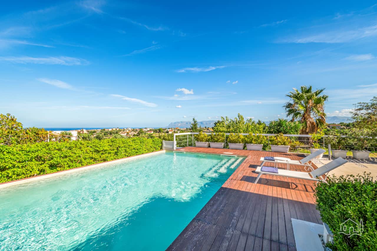 Infinity-style pool with sun loungers, wooden deck, and sweeping sea views on the horizon.