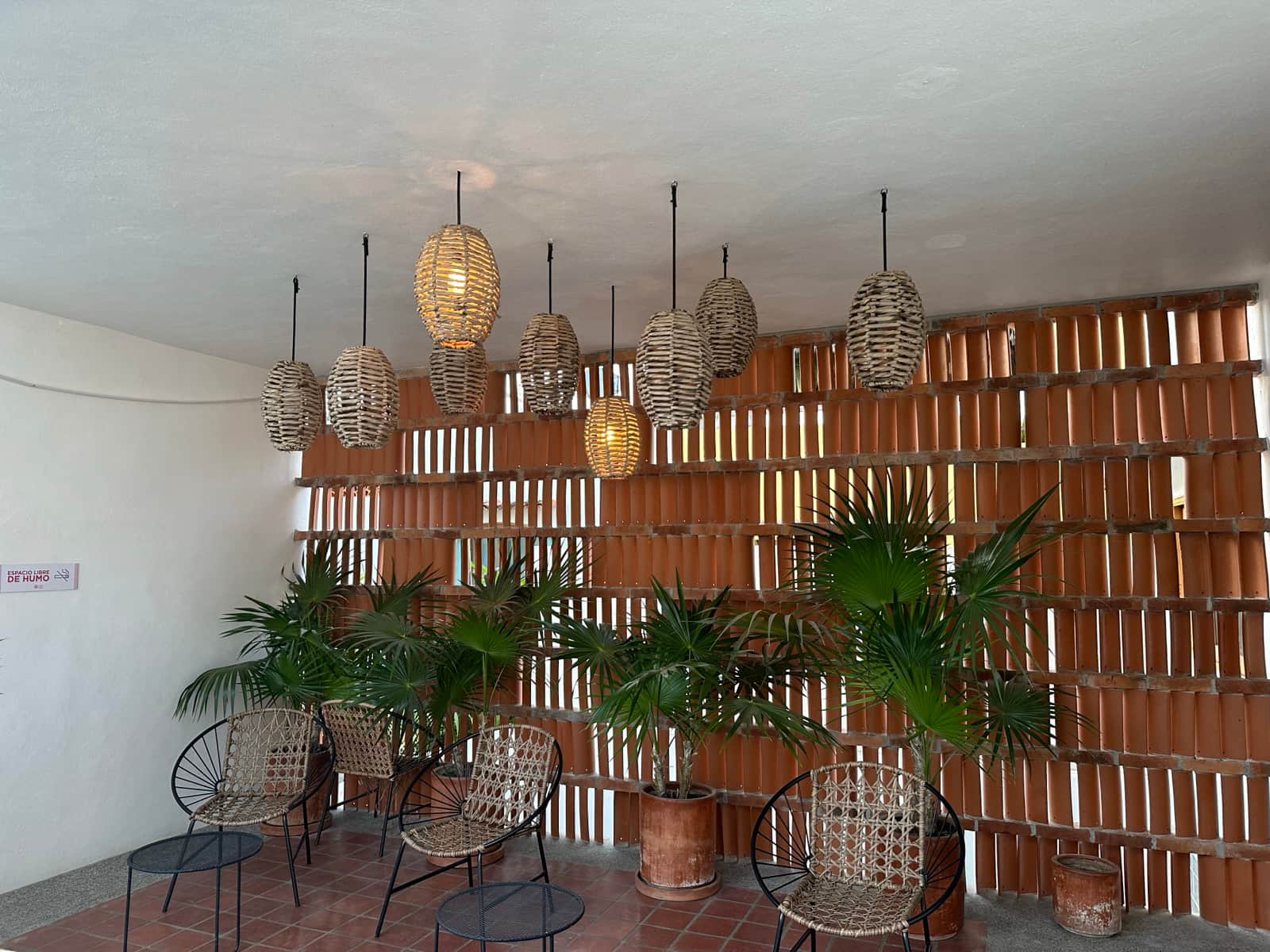 Hotel lounge in San Pancho, Nayarit with woven wicker pendant lamps, a terracotta breeze-block wall, and tropical palms