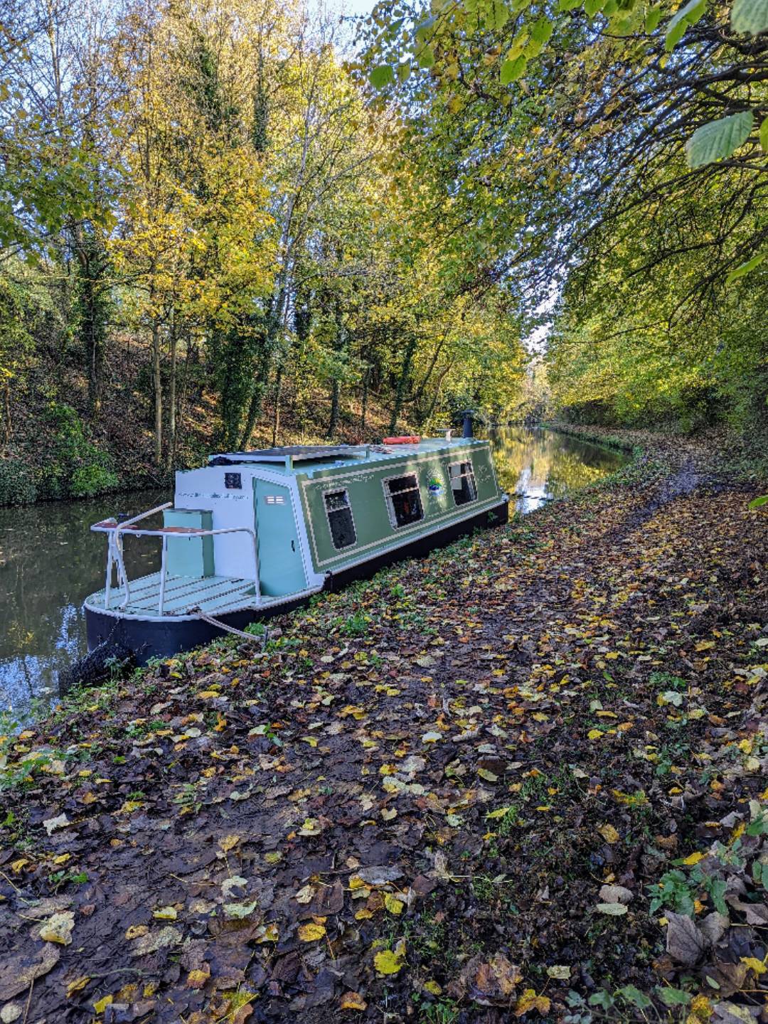 Small canal boat moored under trees in autumn