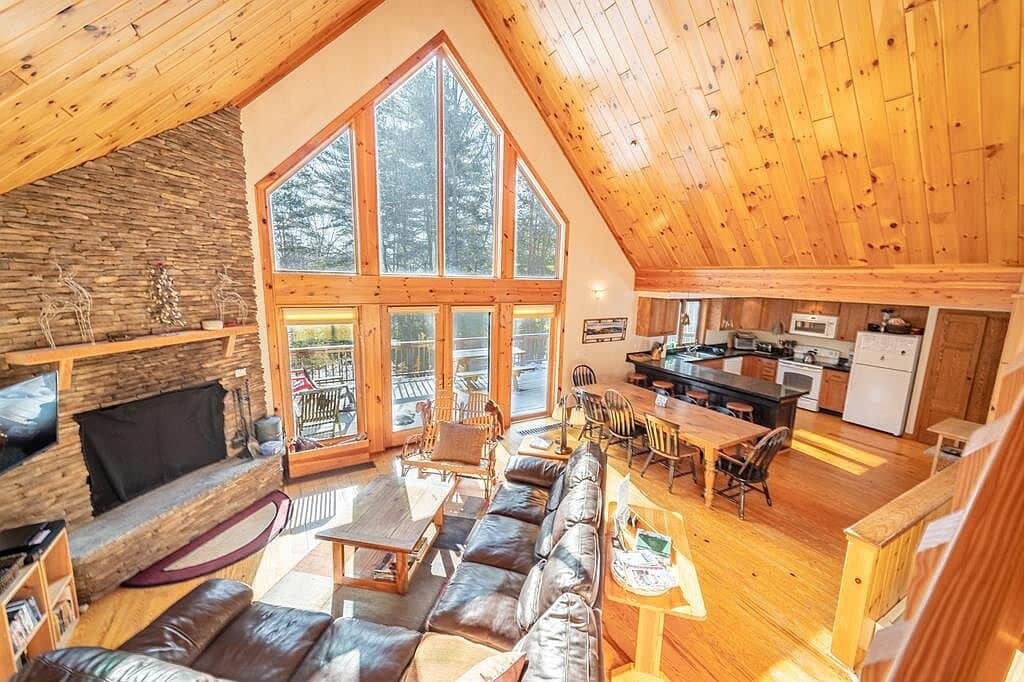 The living room features a soaring cathedral ceiling and a wall of windows that flood the space with natural light. Cozy up by the wood-burning fireplace, enjoy a movie night with Netflix, and stay comfortable year-round with air conditioning