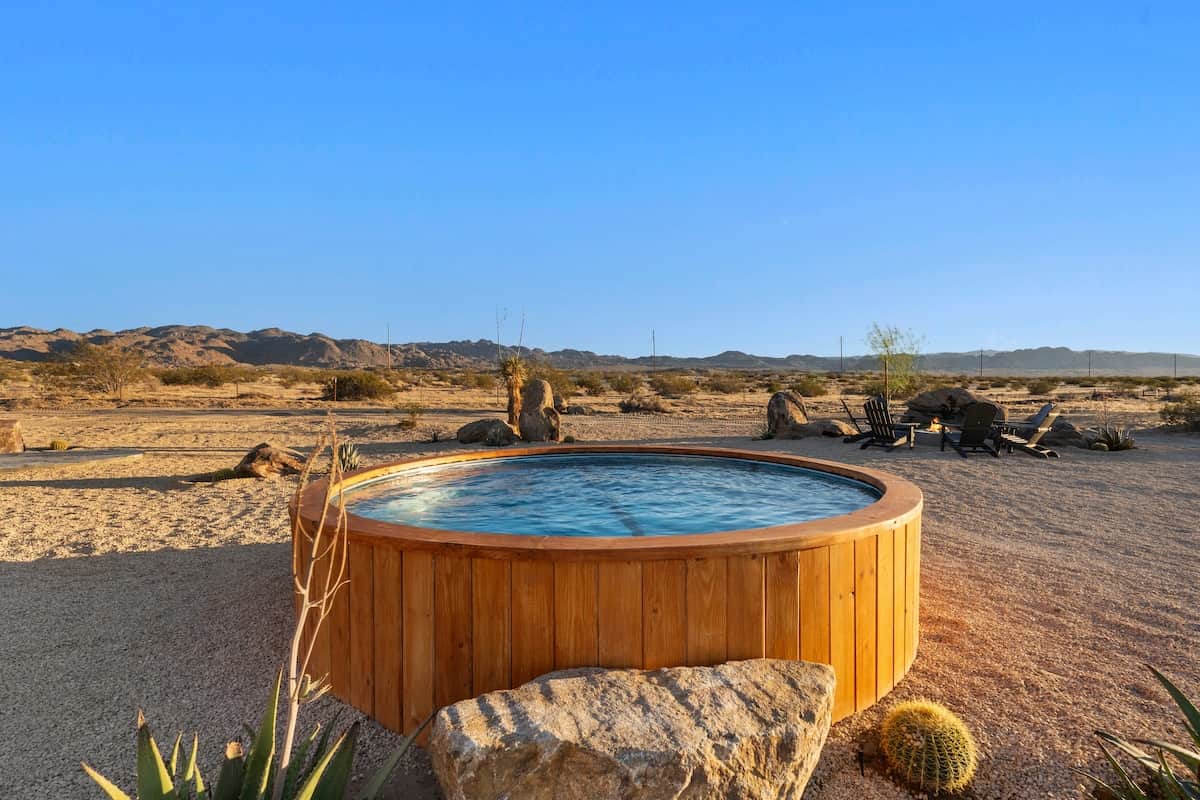 Golden hour at the 10-ft cedar-wrapped cowboy pool — cool water, barrel cactus, and the fire-pit