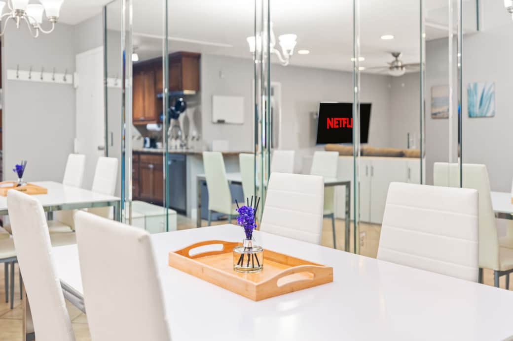 Elegant dining area with mirrored walls, modern lighting, and sleek white furnishings.