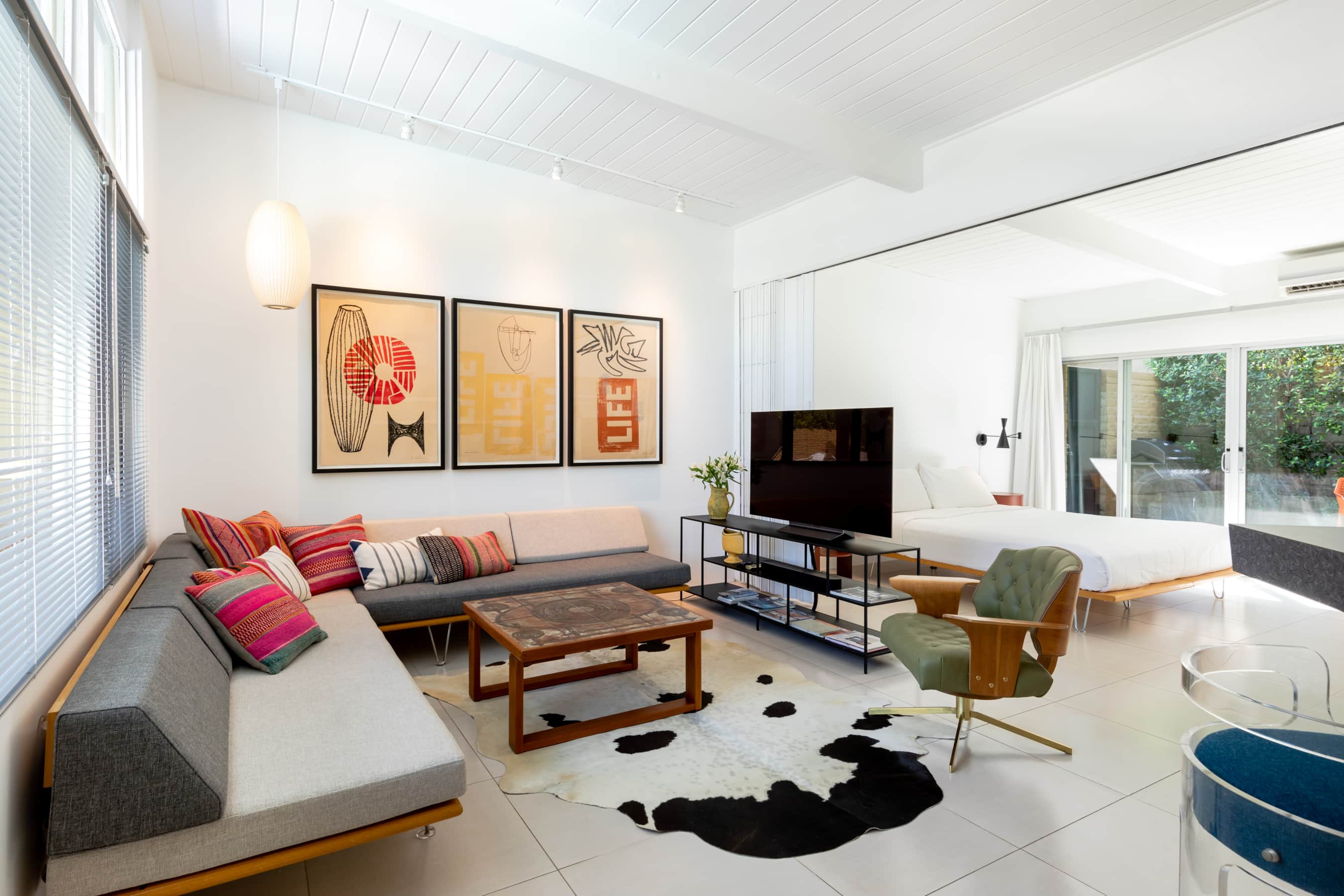 A wide view of a modern living room with a sofa, coffee table, TV, bed, and chair.