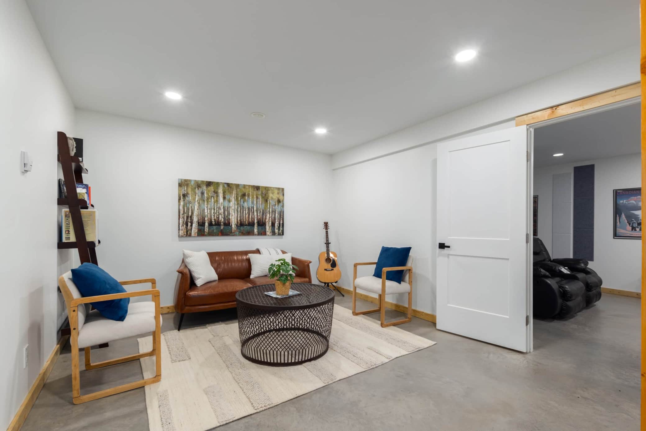 Basement living space with warm finished concrete flooring, custom leather couches, library, and access to theatre.jpg