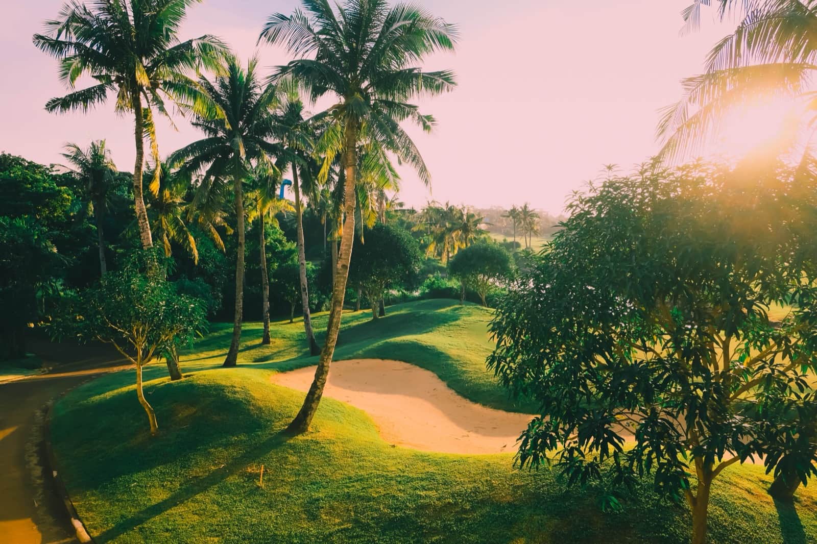 Campo de golf verde con palmeras y trampas de arena bajo un cielo tropical despejado