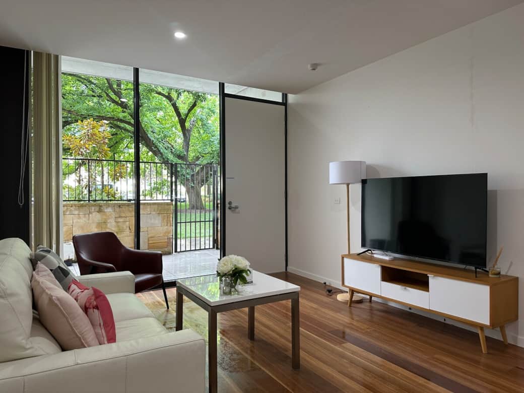 Our spacious living area is designed for comfort and entertainment. With a cozy sofa, a coffee table, and a TV, it's perfect for unwinding. The balcony door provides access to an outdoor space that overlooks lush greenery.