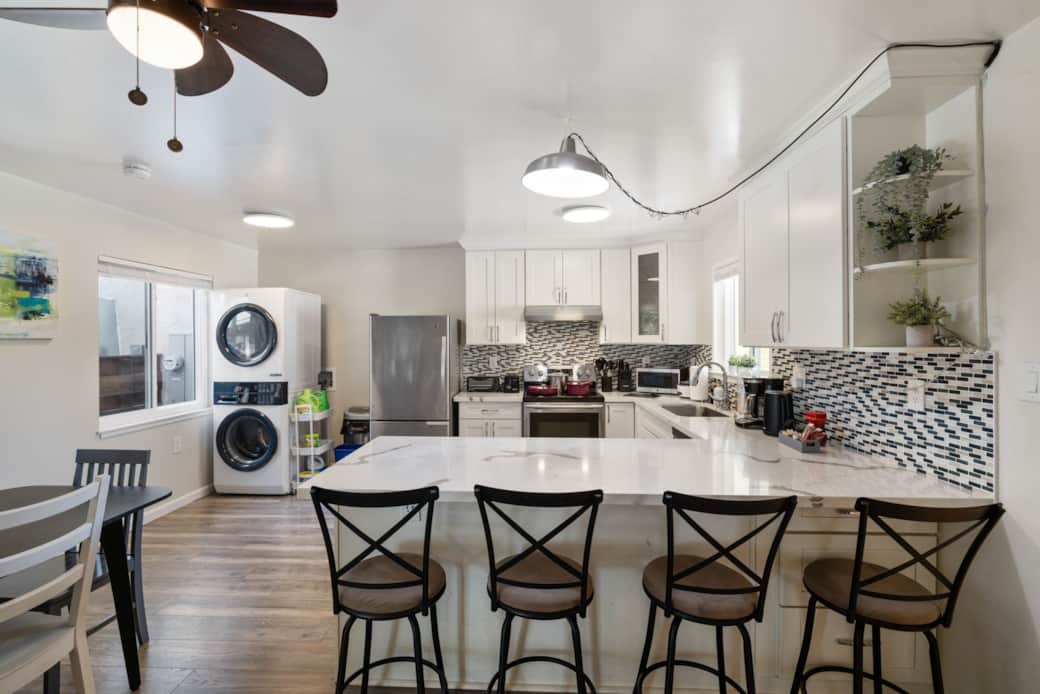 Modern kitchen with island, bar stools, and stacked washer/dryer.