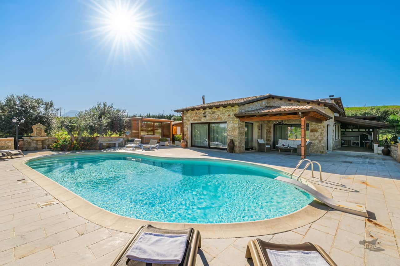 A dreamy pool area with sun loungers, shaded patio, and a relaxing heated hot tub.