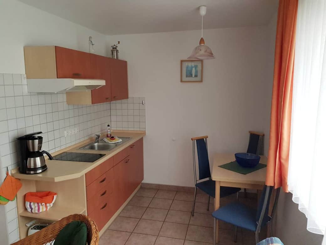 Küchenzeile mit Herd (ohne Backofen) , Kühlschrank ohne Gefrierfach, Kaffeemaschine, Toaster, Wasserkocher, Kochgeschirr, Essgeschirr, Gläser und Besteck sowie Kindergeschirr und -besteck.