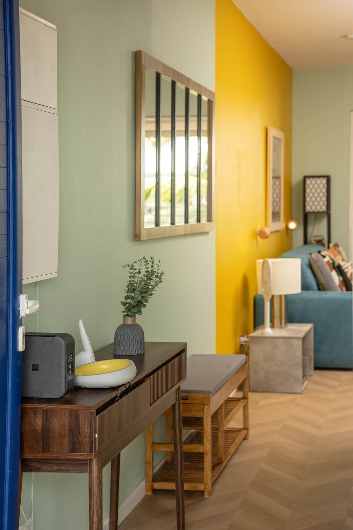 Entrée et bureau avec mur jaune, canapé bleu et accès véranda
