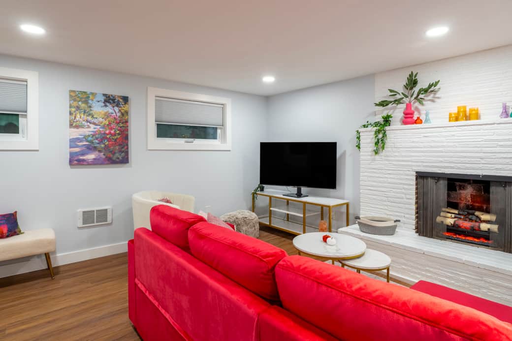 The living room has a modern comfy couch, lots of seating, electric fireplace insert and Smart TV