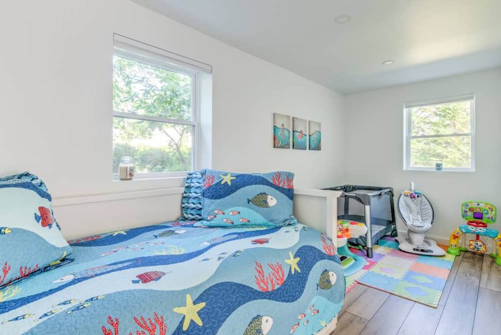 Kids’ playroom with a daybed, toys, a pack ’n play and an infant swing