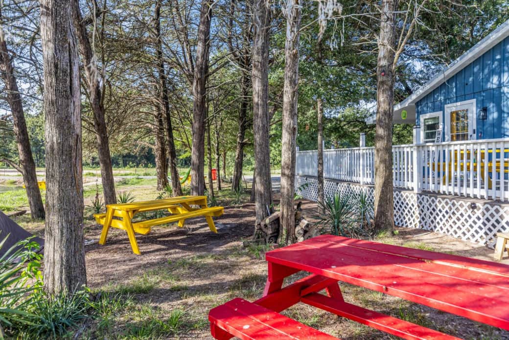 “Colorful picnic tables under the shade of tall trees make the perfect spot for outdoor meals, games, or simply enjoying the fresh country air. A family-friendly gathering place just steps from the farmhouse.”