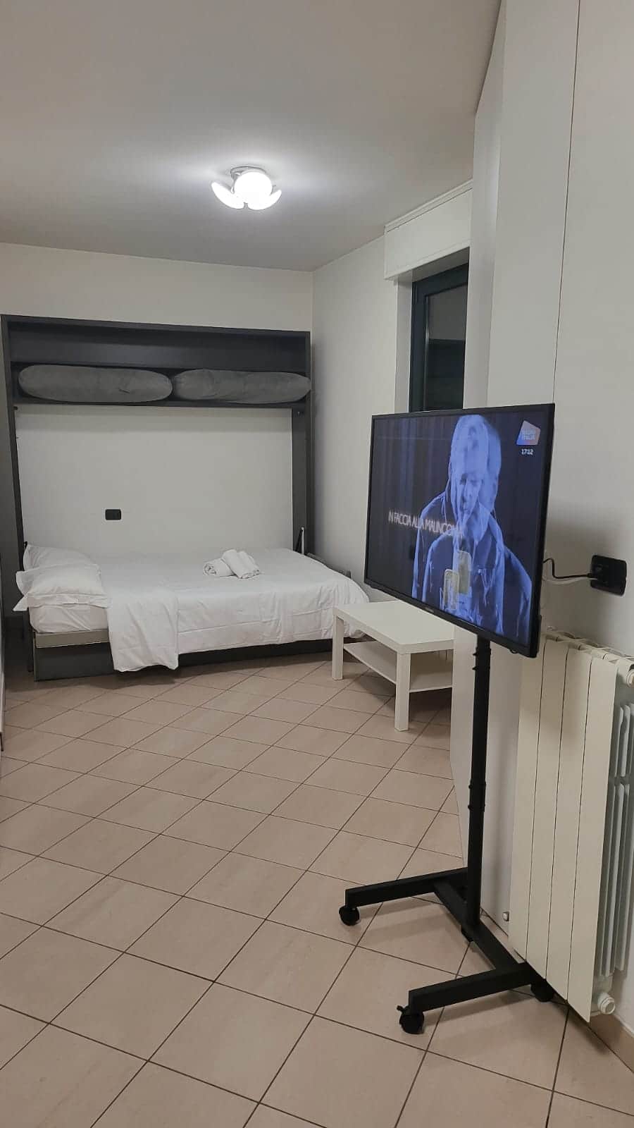 Schlafbereich mit Bett und eingeschaltetem Fernseher
