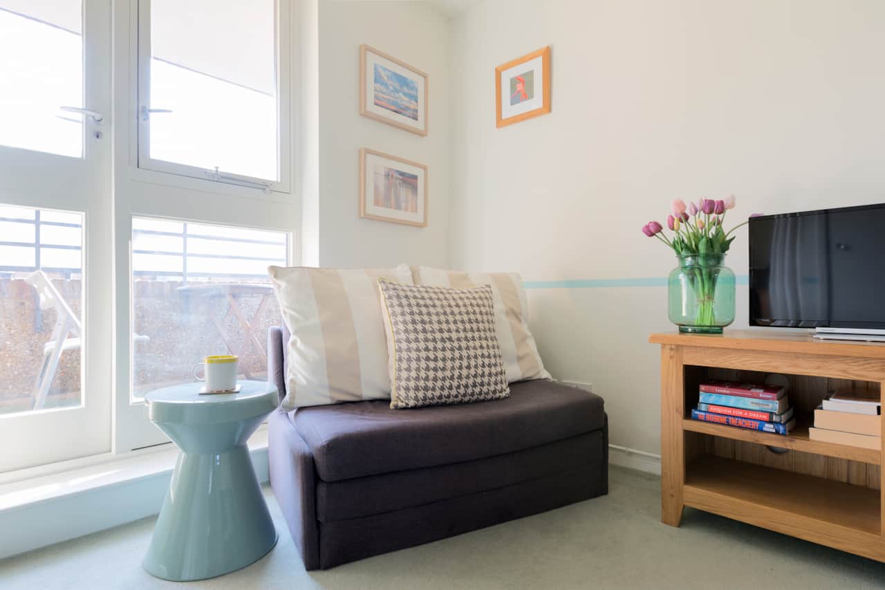 Grey sofa bed beside a ceramic side stool and TV console stocked with books