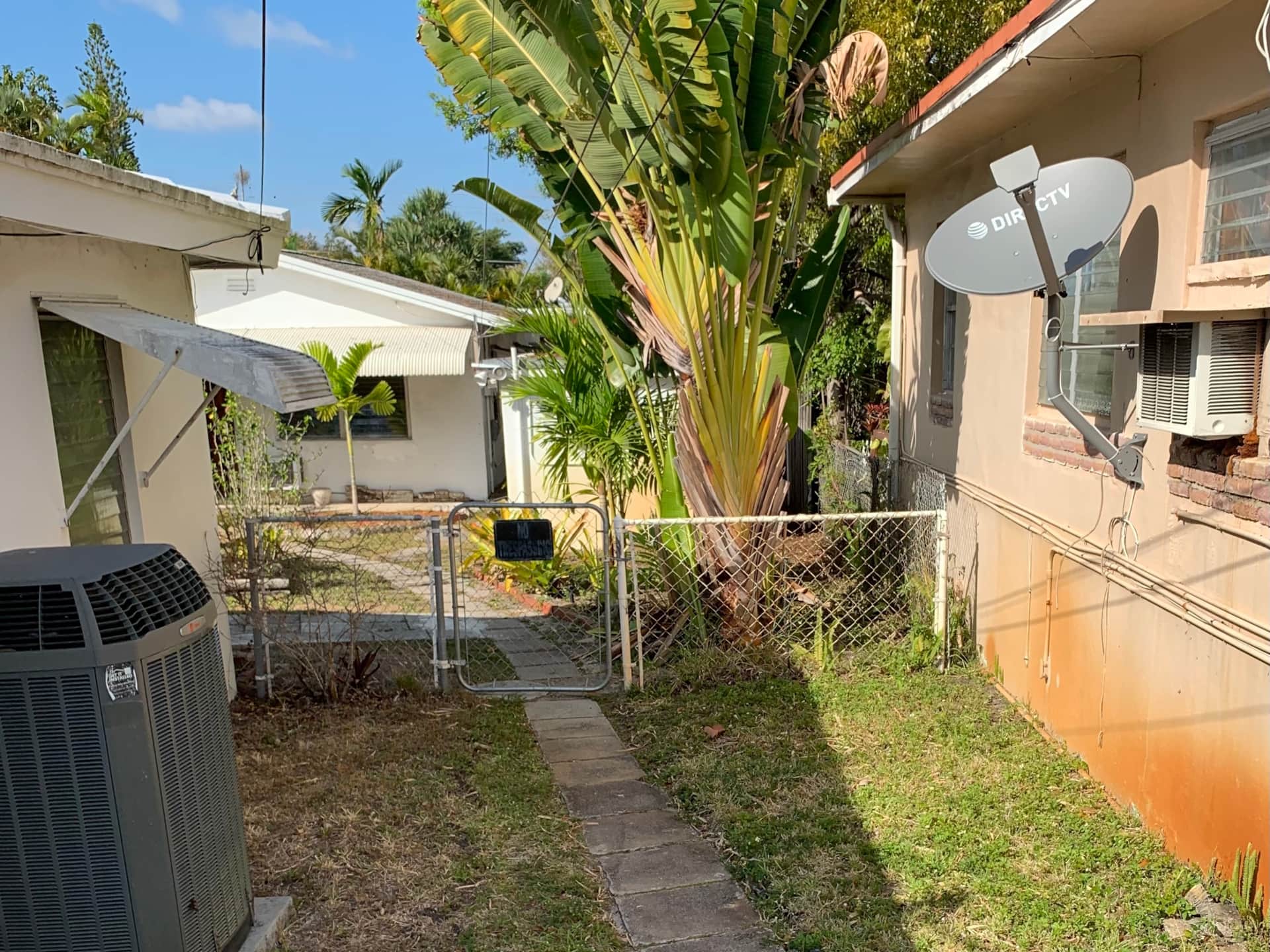 Before renovation entryway at Casa Citron showing exposed electrical wires on the ground, chain-link fence, and lack of privacy or defined entrance.