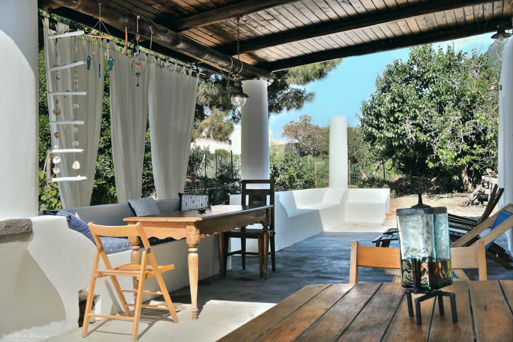 Terrazza arredata con tavolo, sedute e tende bianche nella Casa del Gelso Bianco a Salina