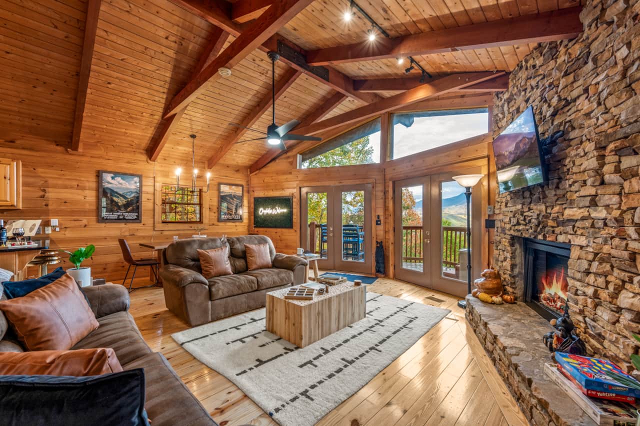 Cozy cabin living room with fireplace, tall windows and mountain views
