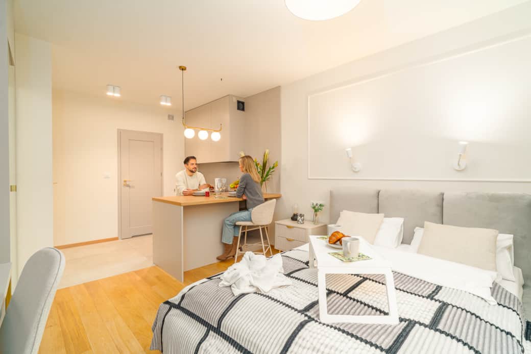 An attractive studio apartment with a kitchenette, a large bed, and bright lighting.