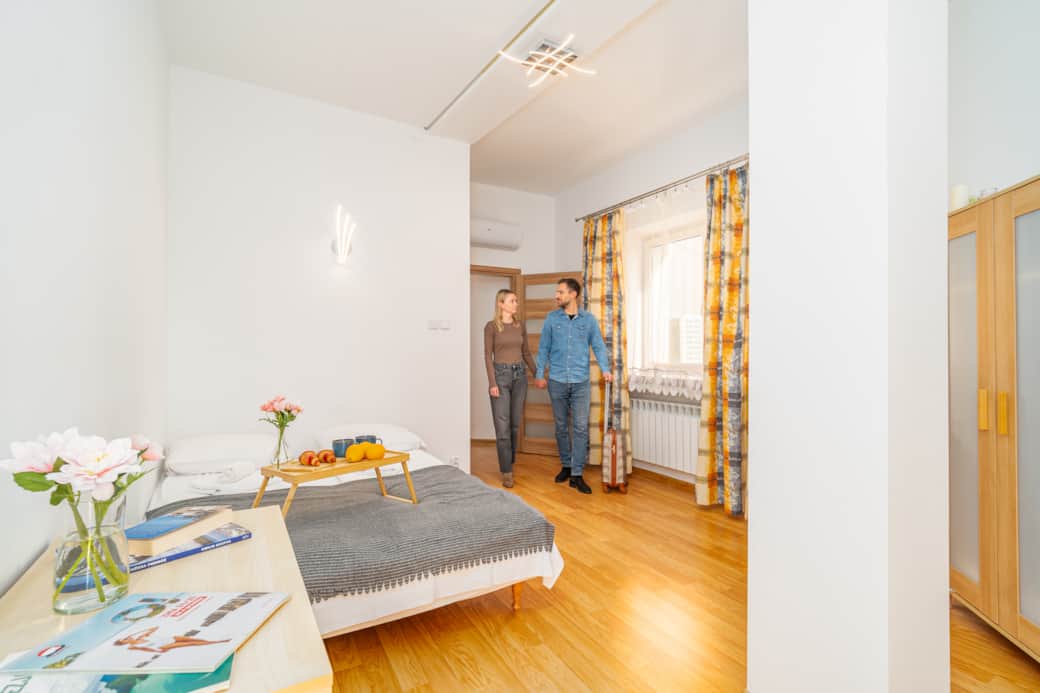 Przytulna, jasna sypialnia z drewnianą podłogą i dużym oknem.