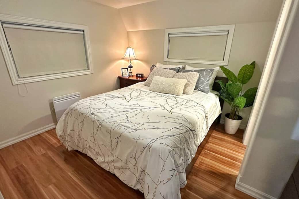 Bright and peaceful queen bedroom with soft bedding and room-darkening blinds for restful sleep.