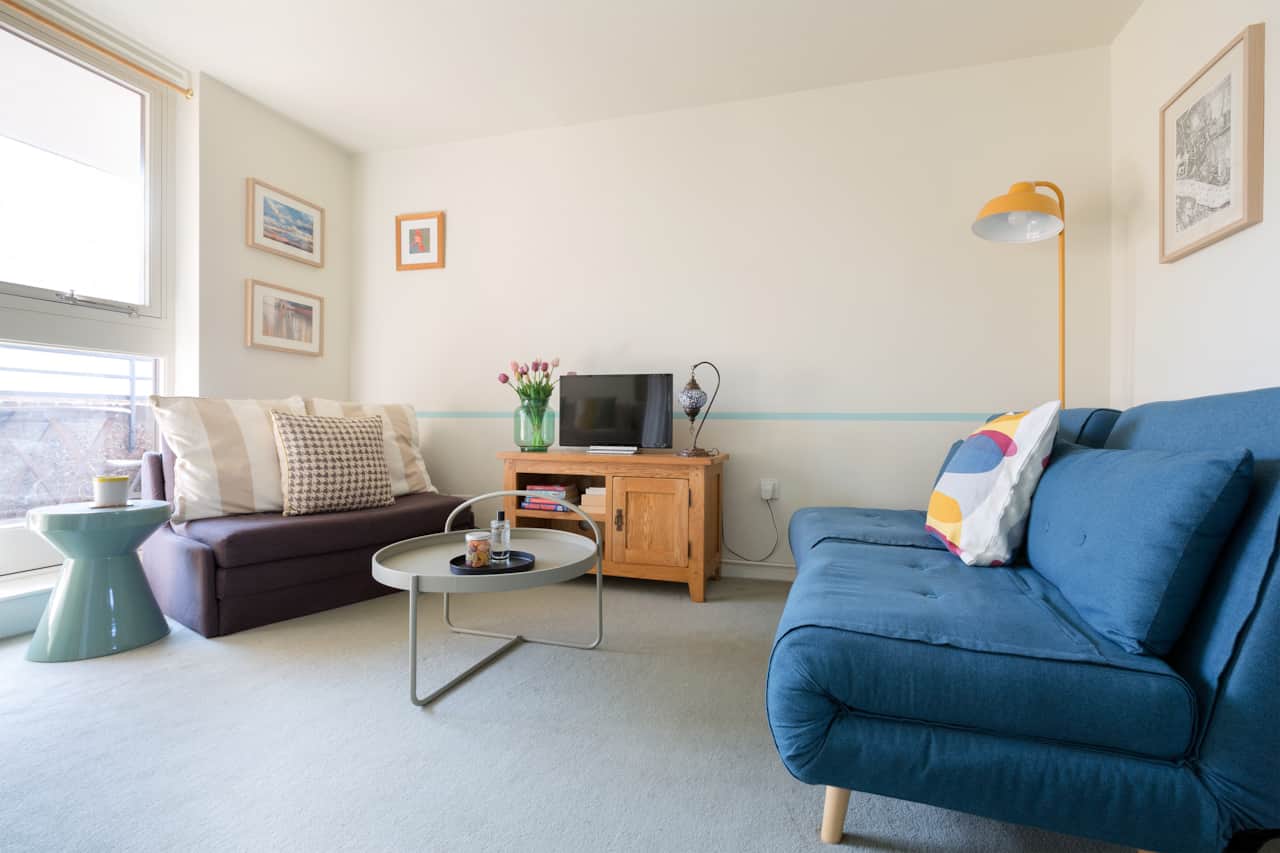 Bright open-plan lounge with sofa bed, day bed, TV and colourful gallery wall