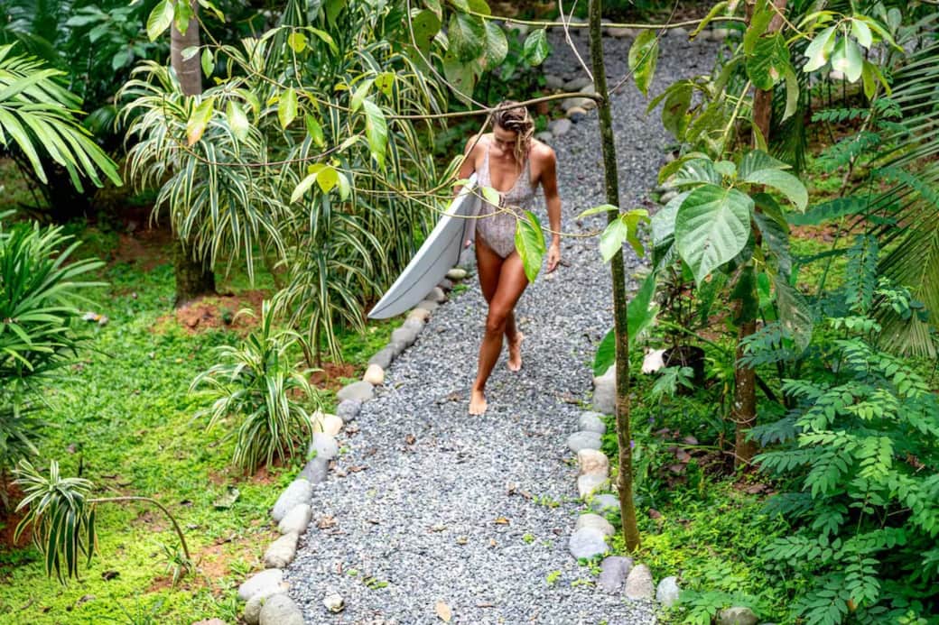 Surfer girl carrying her board up the lush jungle path leading to the Monkey Treehouse. Capturing the tropical lifestyle of Big Creek, Bocas del Toro—where adventure, surf, and nature meet at your doorstep.