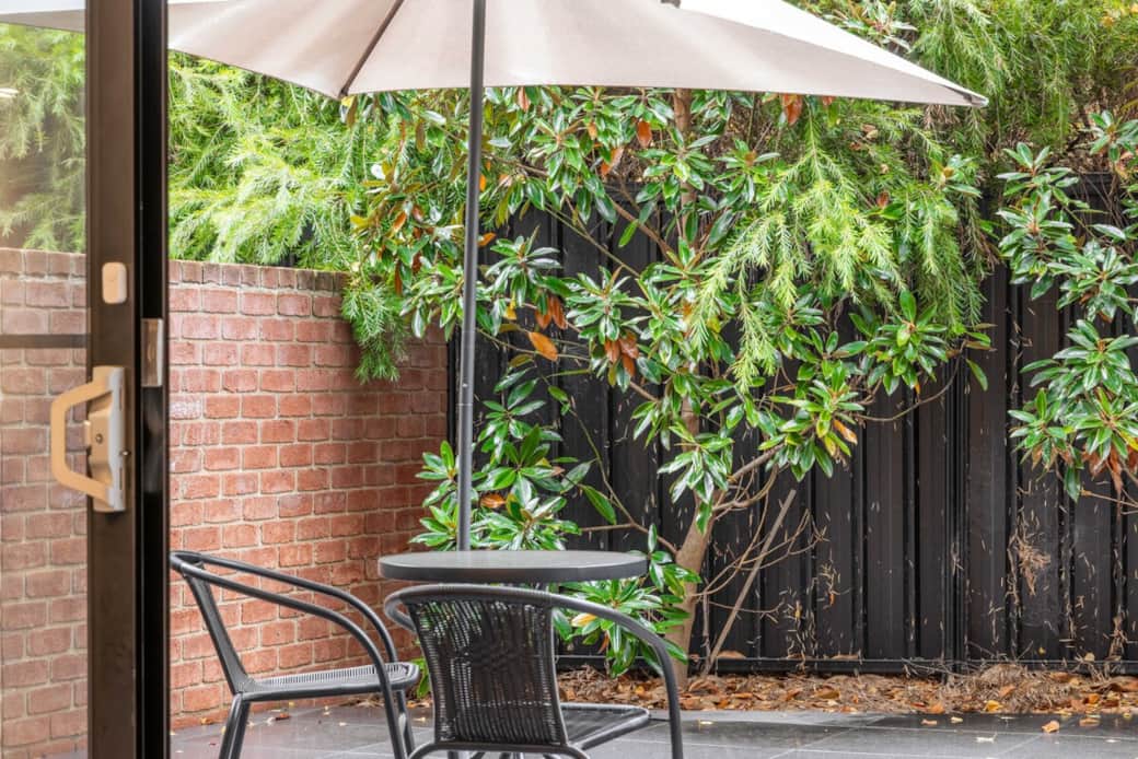 Retreat to your private outdoor oasis, featuring a comfortable patio set under a large umbrella. The lush greenery and black fence offer privacy and serenity. It's the perfect spot for morning coffee or an evening relax after a day of exploration.