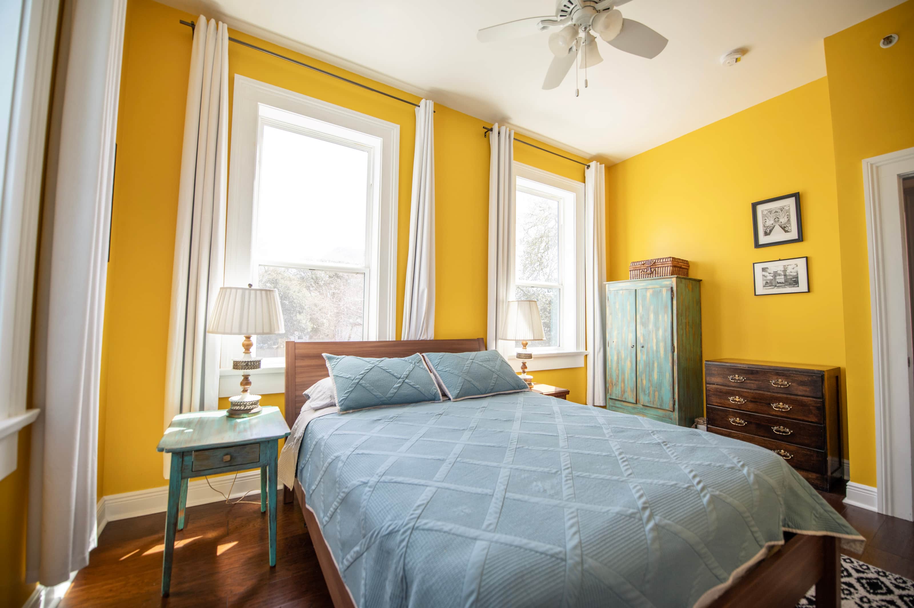 A bright guest room with yellow walls, a double bed, and two windows.