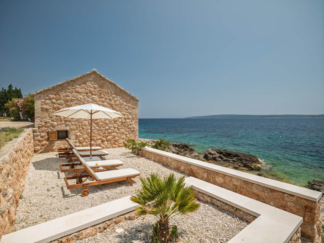 Traditional stone house at Bogić Kuća with sun loungers and a white umbrella facing the sea.
