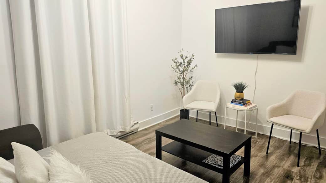 Cozy living room with seating area, wall-mounted TV, and minimalist decor in a main-floor apartment Cozy living room with seating area, wall-mounted TV, and minimalist decor in a main-floor apartment