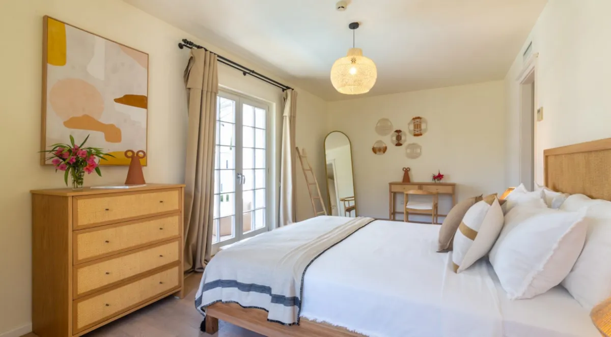 Bedroom with a double bed, dresser, and a small table, featuring a large mirror and decorative wall art.