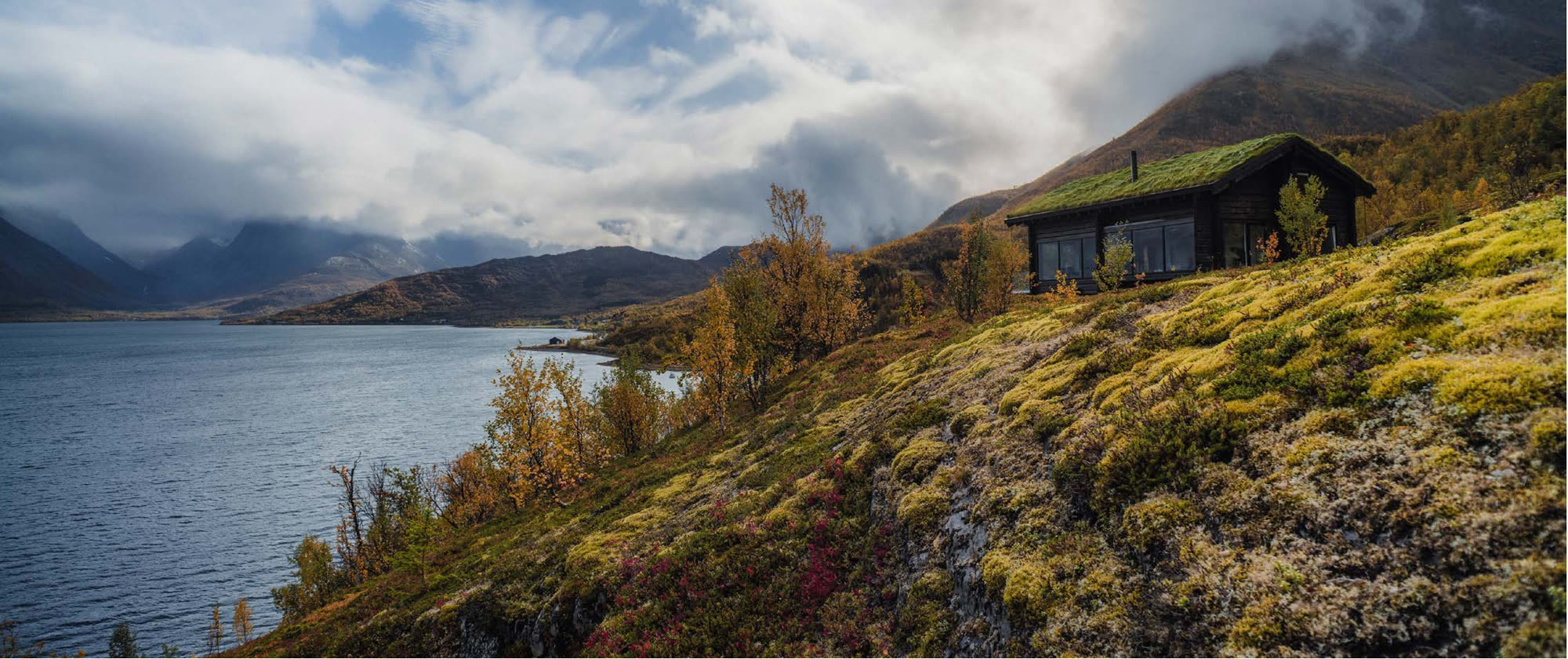 Log chalet with turf roof above the fjord in autumn